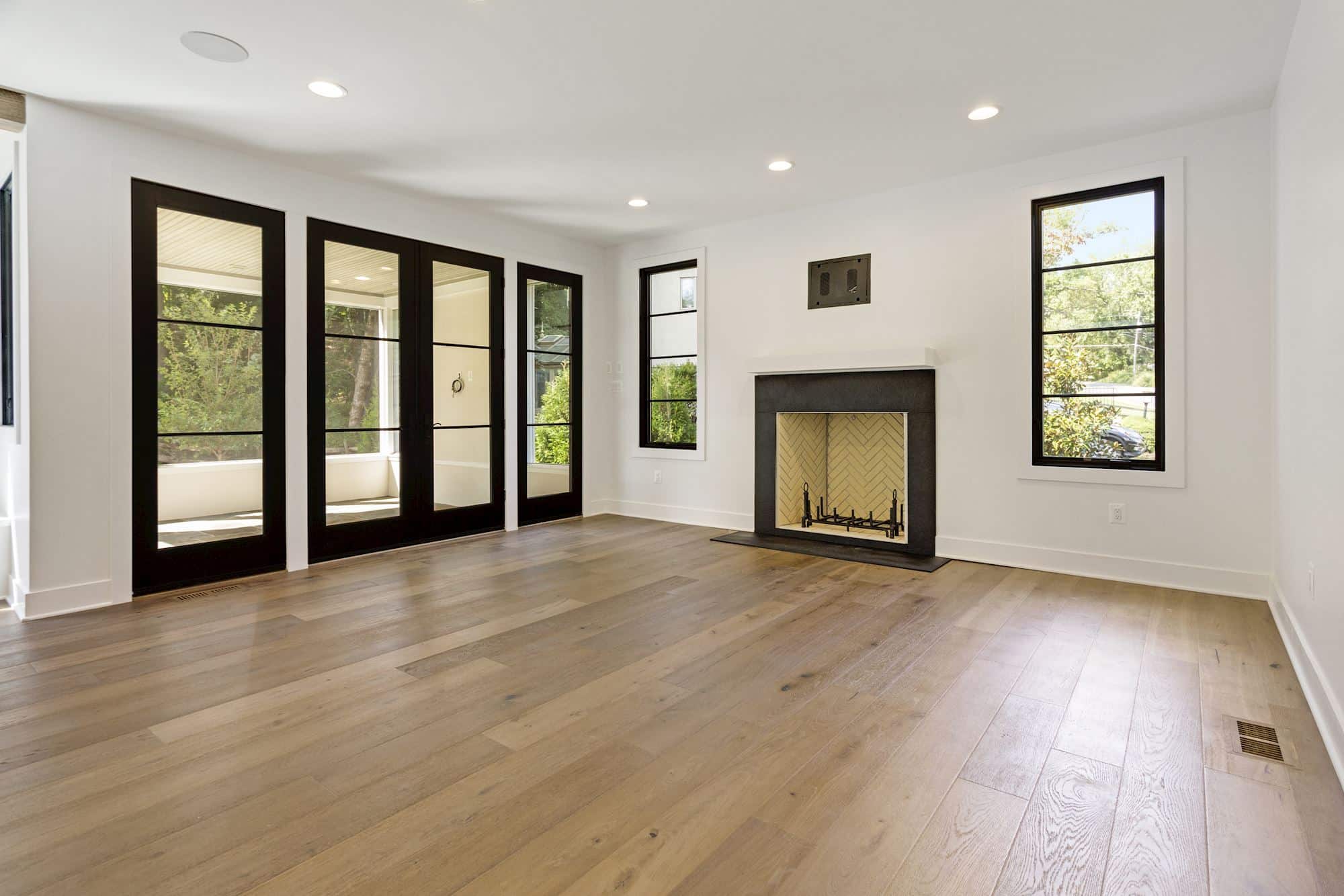 Sunlit living room glows with herringbone fireplace and French doors.