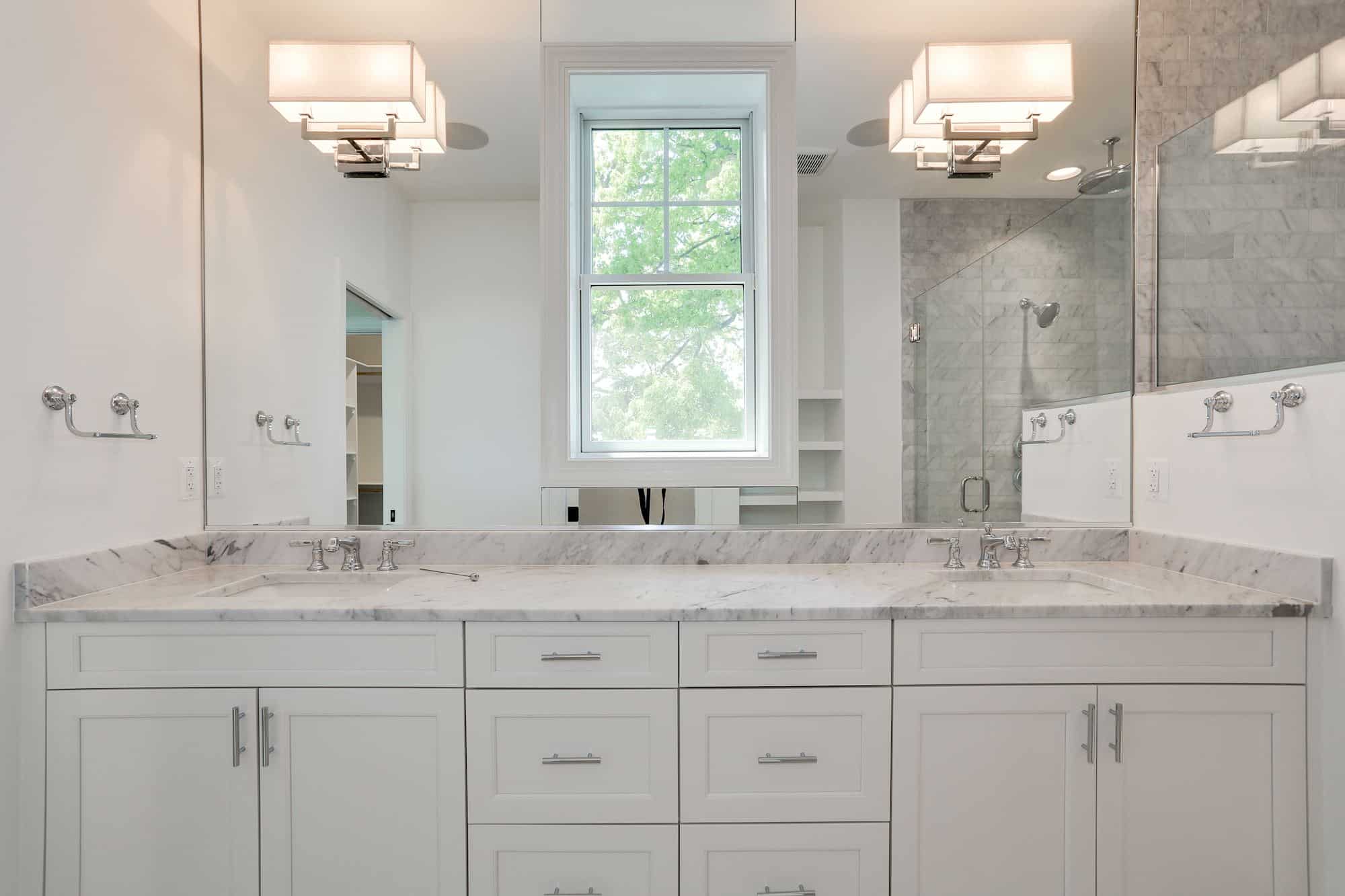 Primary bath with marble vanity, frameless shower, and natural light