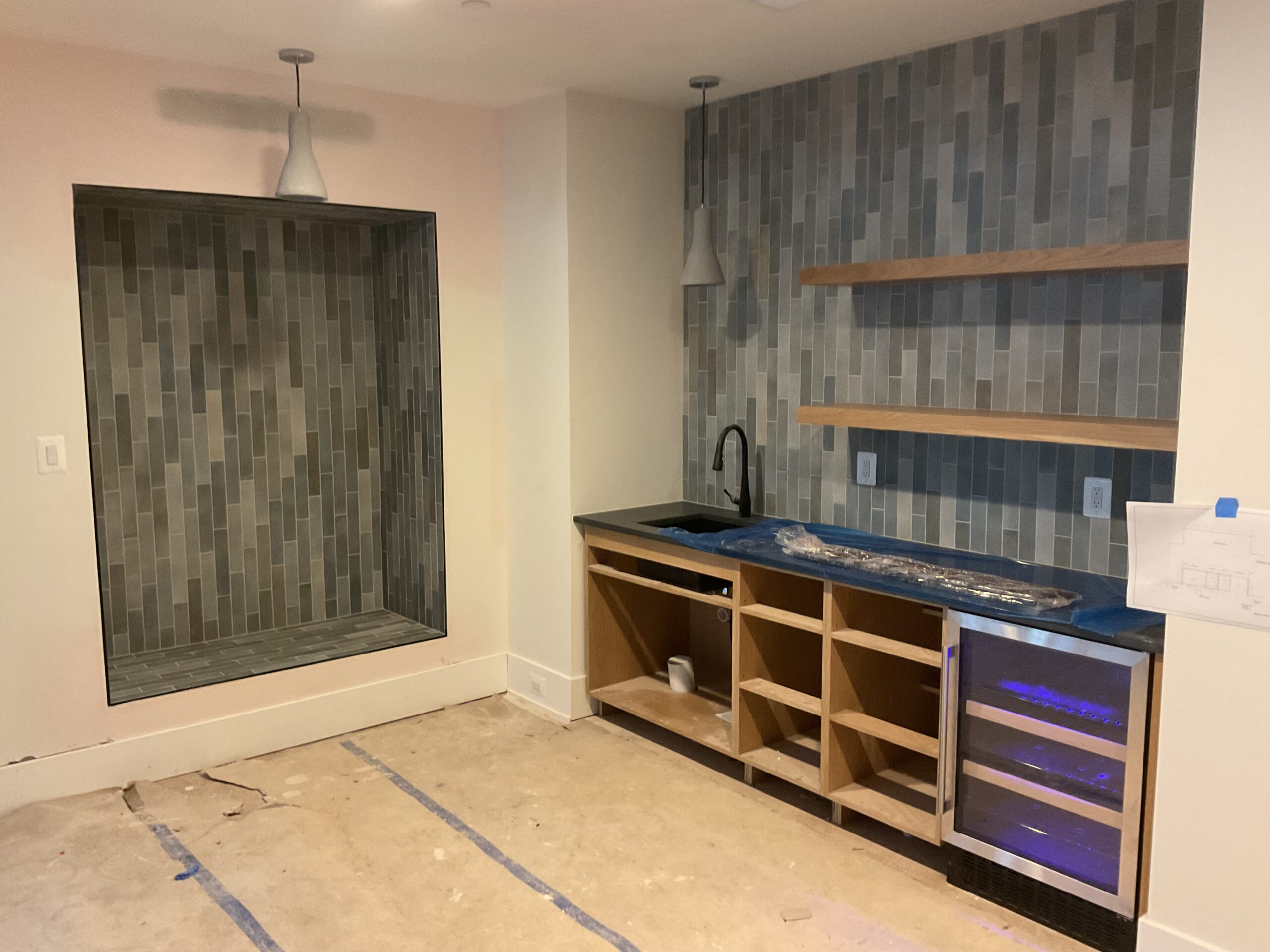 Architectural tile accent wall, wine fridge, custom shelving. The basement level where Friday nights stay downstairs.